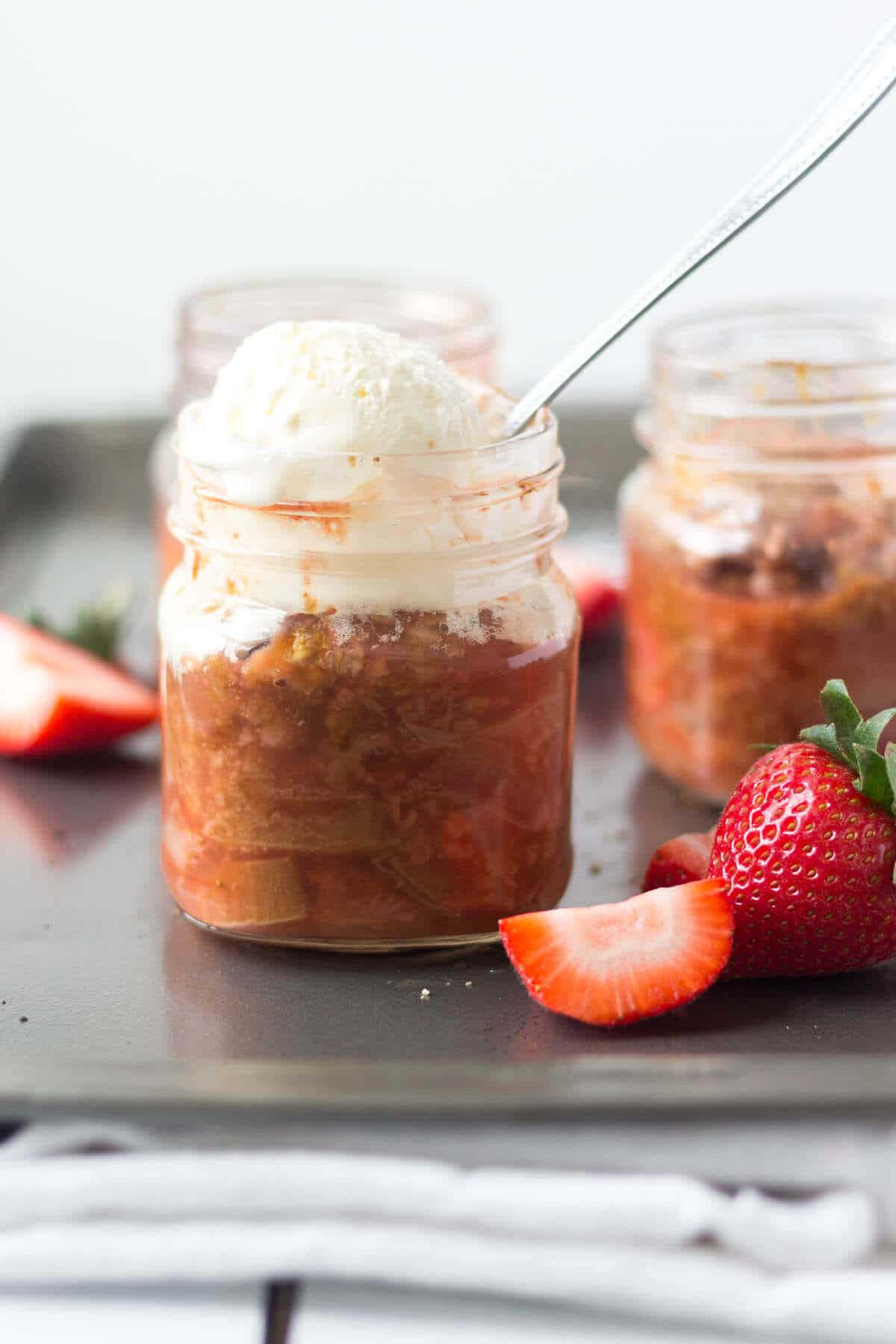 strawberry rhubarb crisp in a small glass mason jar with whipped cream frosting and a silver spoon in it