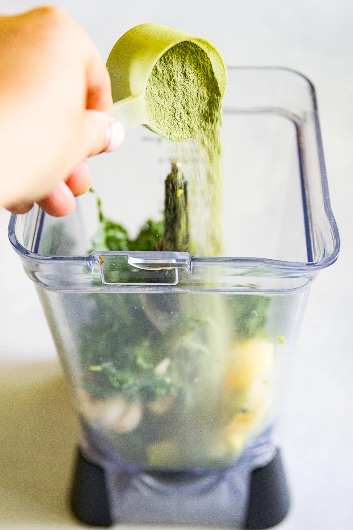 hand dumping matcha from a protein scoop into a blender full of ingredients for a green smoothie bowl recipe