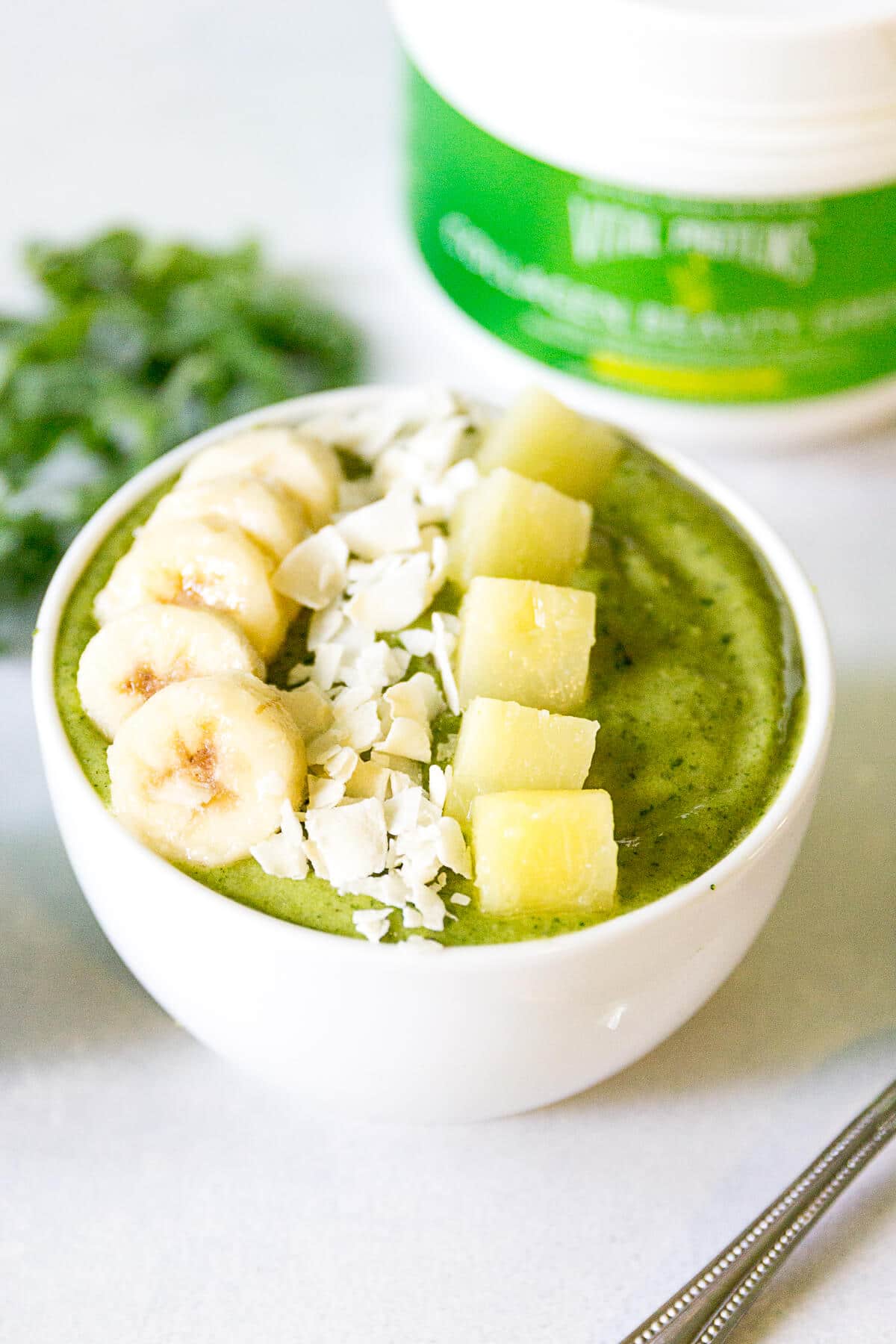 green smoothie bowl recipe in a white bowl and topped with banana slices, coconut flakes and banana chunks