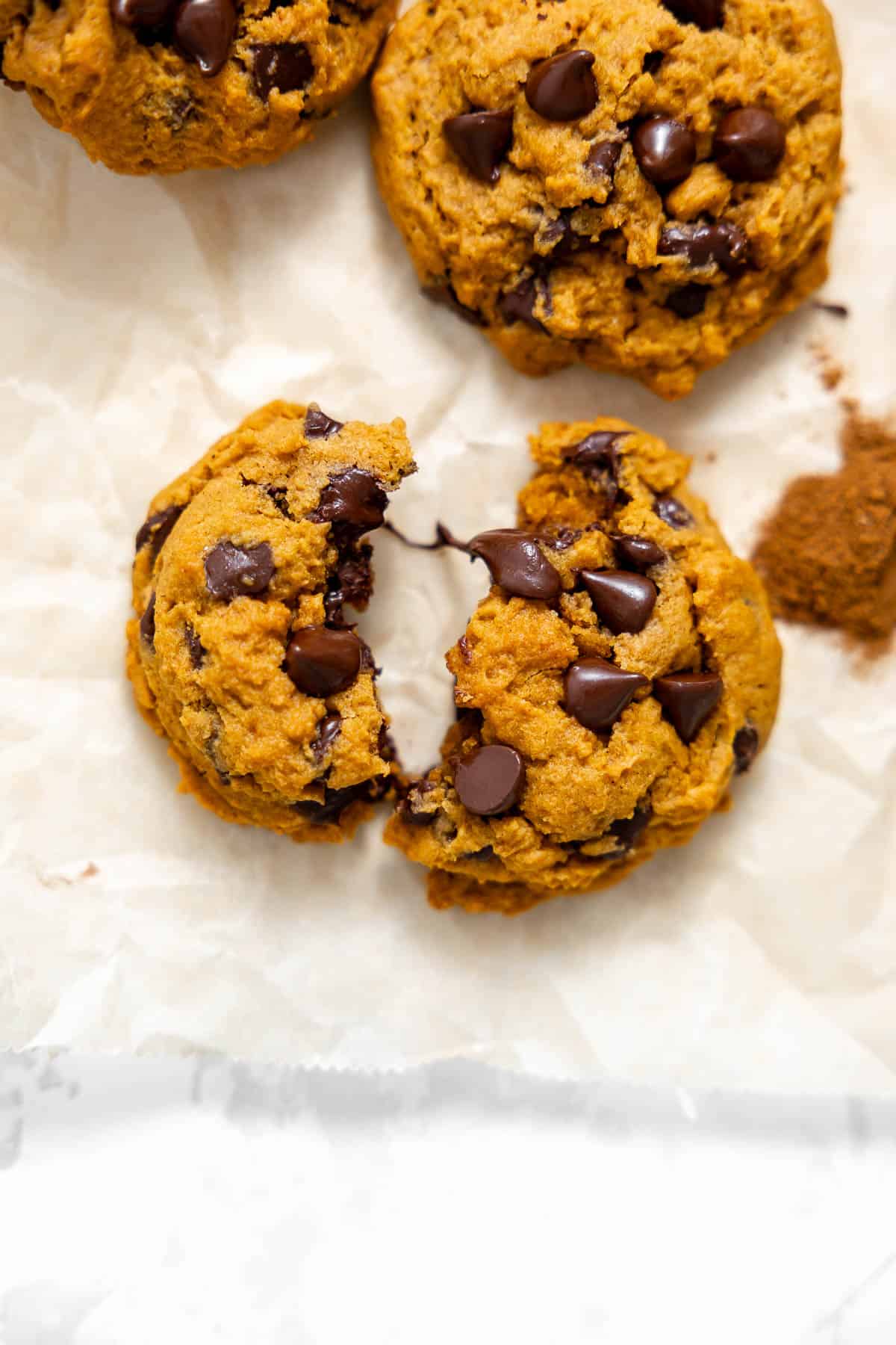 a pumpkin pudding cookie broken in half on a piece of parchment paper.