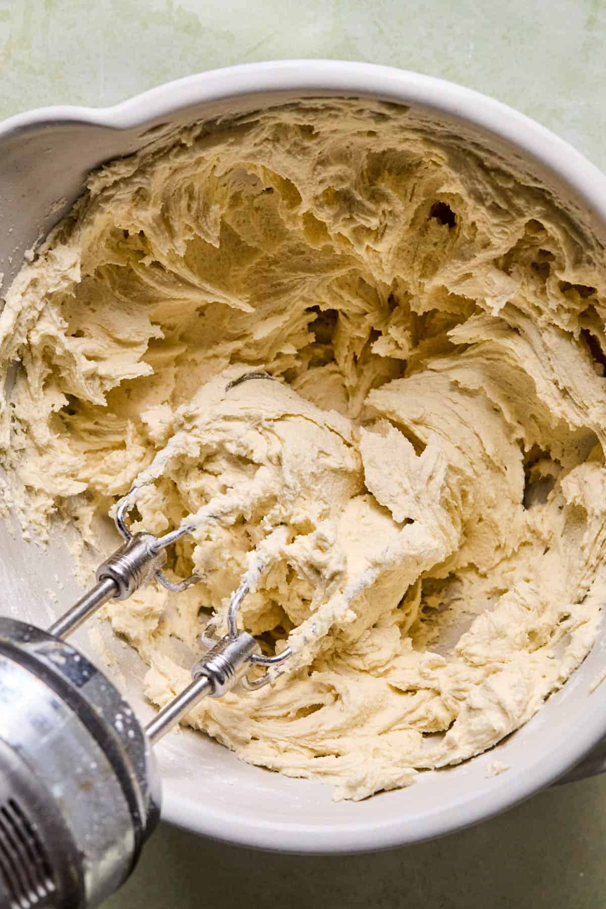 melting moments cookie dough mixed in a bowl with an electric mixer.