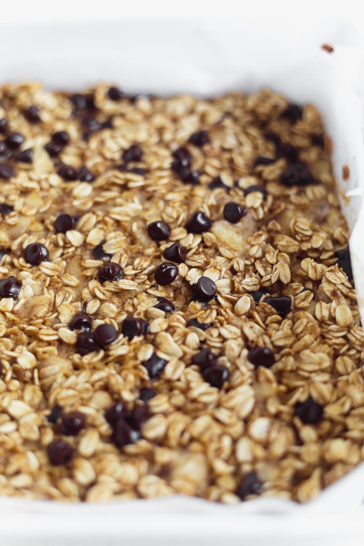 baked oatmeal with banana and chocolate chips in a white 8x8 inch baking dish