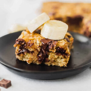 a piece of banana baked oatmeal on a black dessert plate with melted chocolate chips and banana