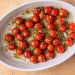 cherry tomatoes in a baking dish with olive oil, garlic, and pesto