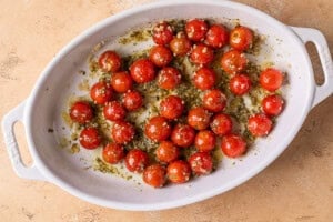 cherry tomatoes in a baking dish with olive oil, garlic, and pesto