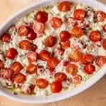 caprese cheese dip topped with sliced tomatoes before baking