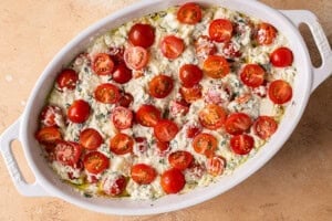 caprese cheese dip topped with sliced tomatoes before baking
