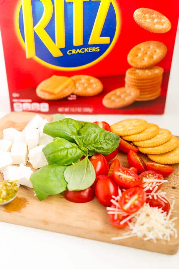 fresh basil, mozzarella, diced grape tomatoes, grated parmesan, pesto and ritz crackers on a cutting board