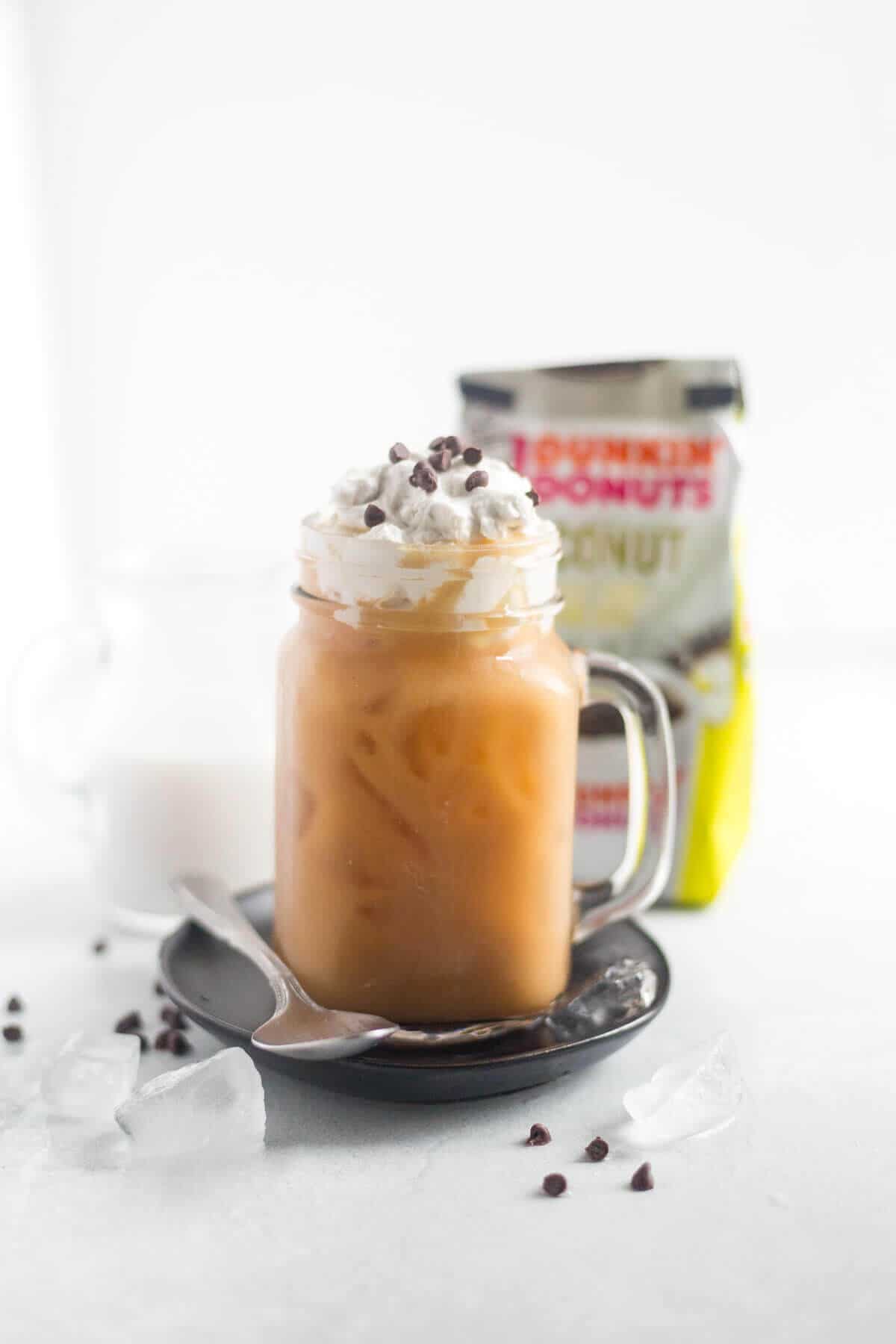 mocha iced coffee topped with whipped cream and chocolate chips in a glass mug resting on a small plate with a spoon