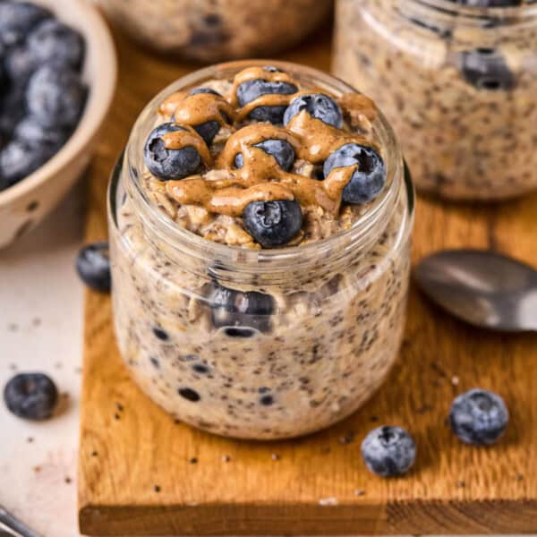 a jar of blueberry overnight oats on a wood table with blueberries and almond butter on top.