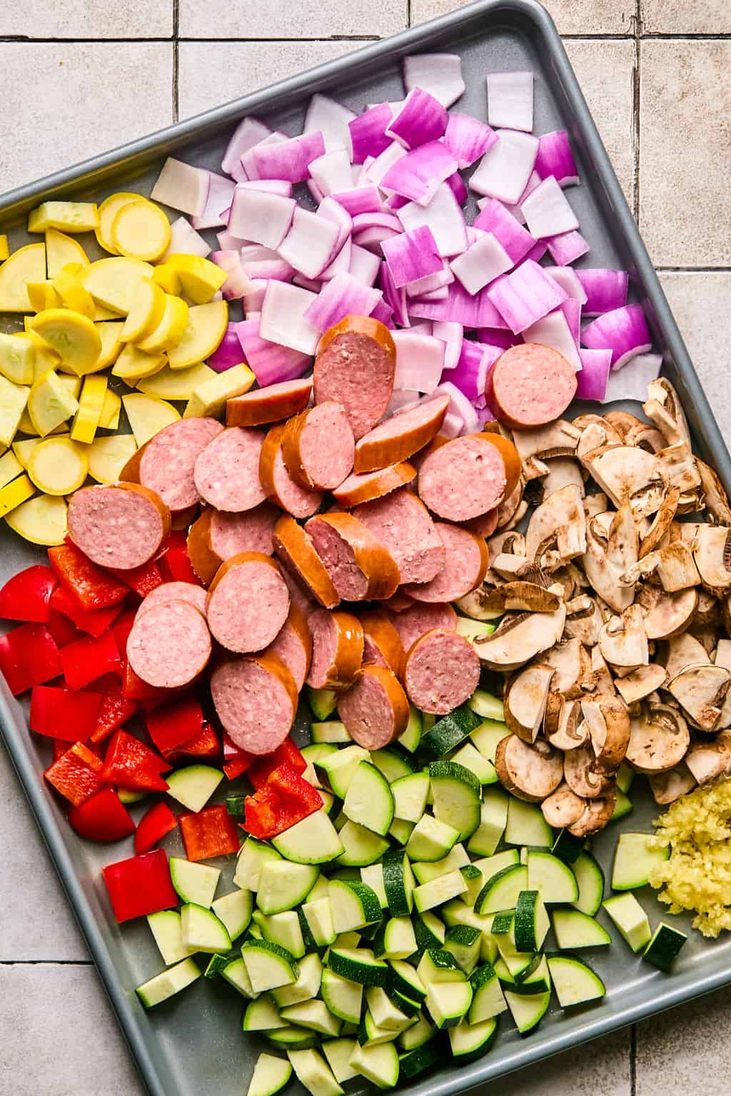 chopped vegetables and smoked sausage on a sheet pan.