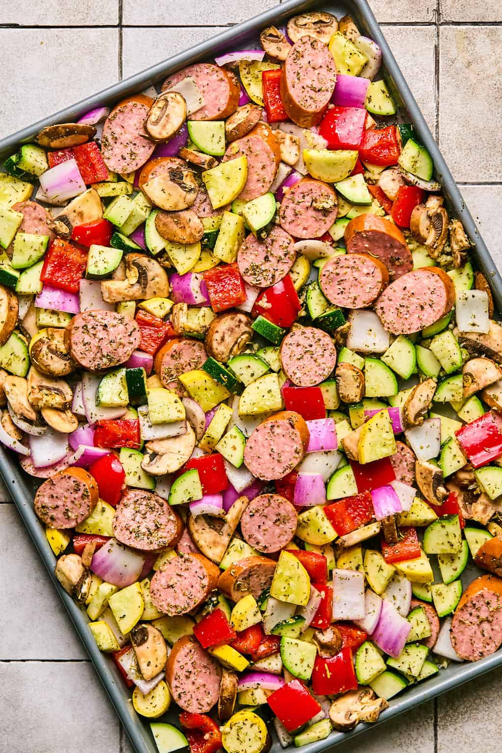 uncooked sausage and veggies on a sheet pan with seasoning.