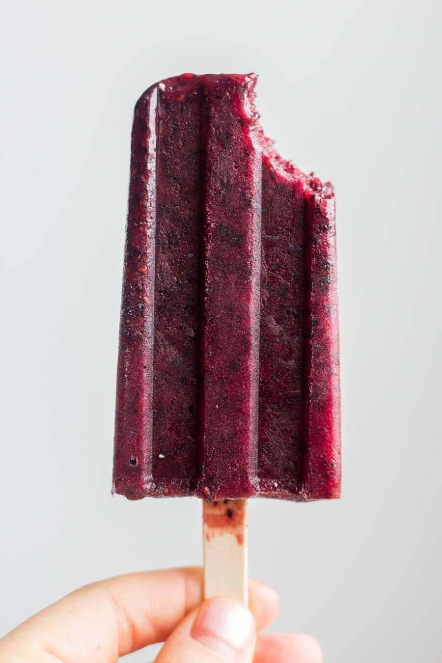 a hand holding up a homemade healthy blueberry popsicle with a bite taken out of the corner