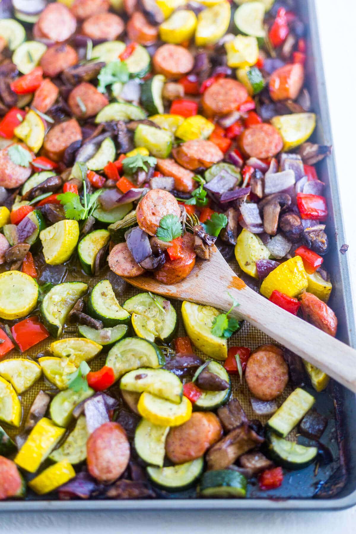 one pan sausage and veggies with a wooden spoon scooping some off the pan