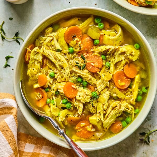 Bowl of PCOS-friendly chicken soup filled with shredded chicken, carrots, celery, peas, and brown rice in a golden turmeric broth, garnished with fresh thyme and served with a spoon.