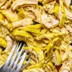 Shredded turmeric-seasoned chicken on a cutting board with a fork, prepared for chicken soup.