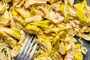 Shredded turmeric-seasoned chicken on a cutting board with a fork, prepared for chicken soup.