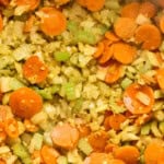 Sautéed carrots, celery, onion, and garlic in a pot, forming the aromatic base for chicken soup.