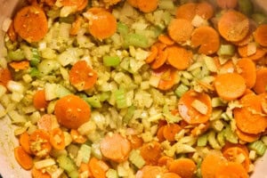 Sautéed carrots, celery, onion, and garlic in a pot, forming the aromatic base for chicken soup.