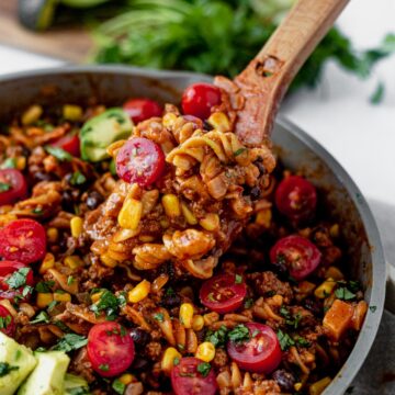 One pot taco pasta topped with tomatoes and avocado in a skillet
