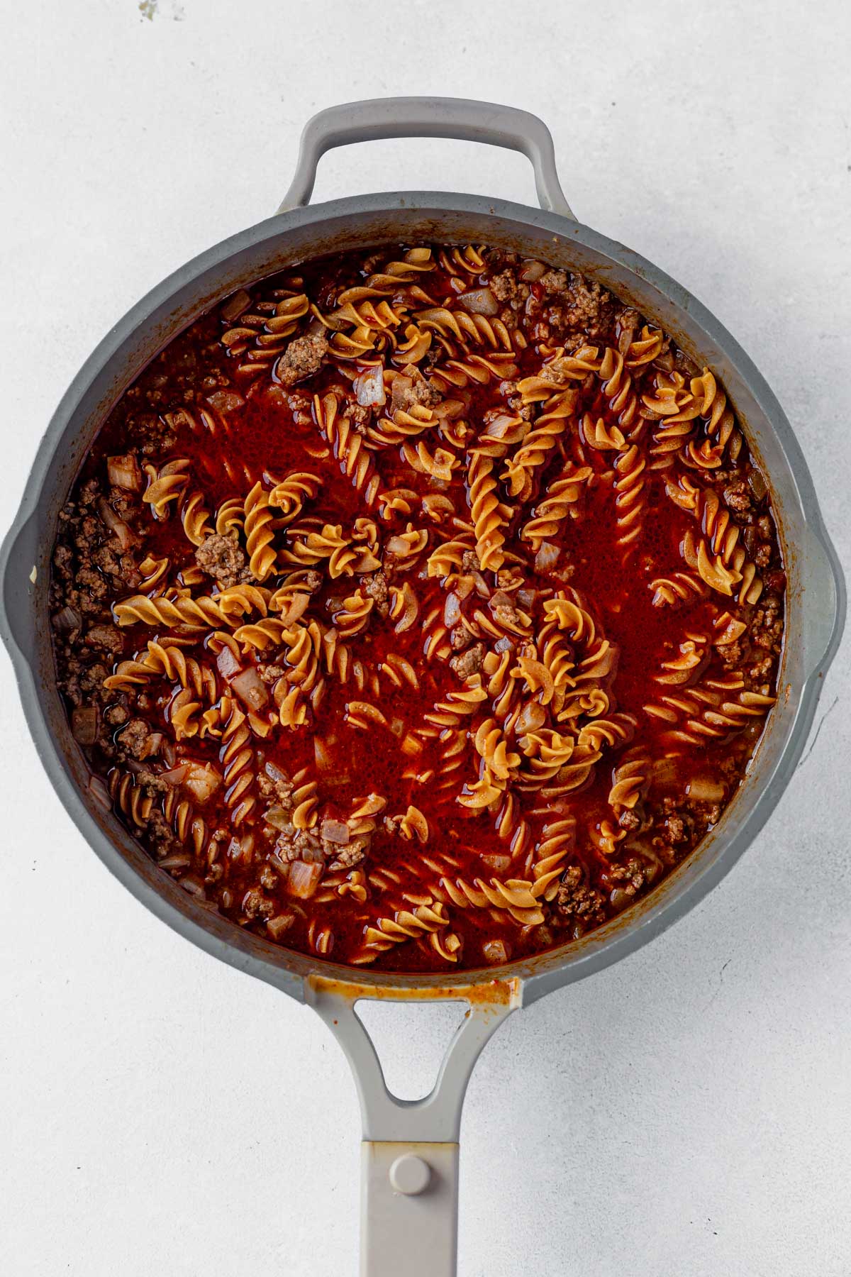 beef and uncooked taco pasta in a skillet