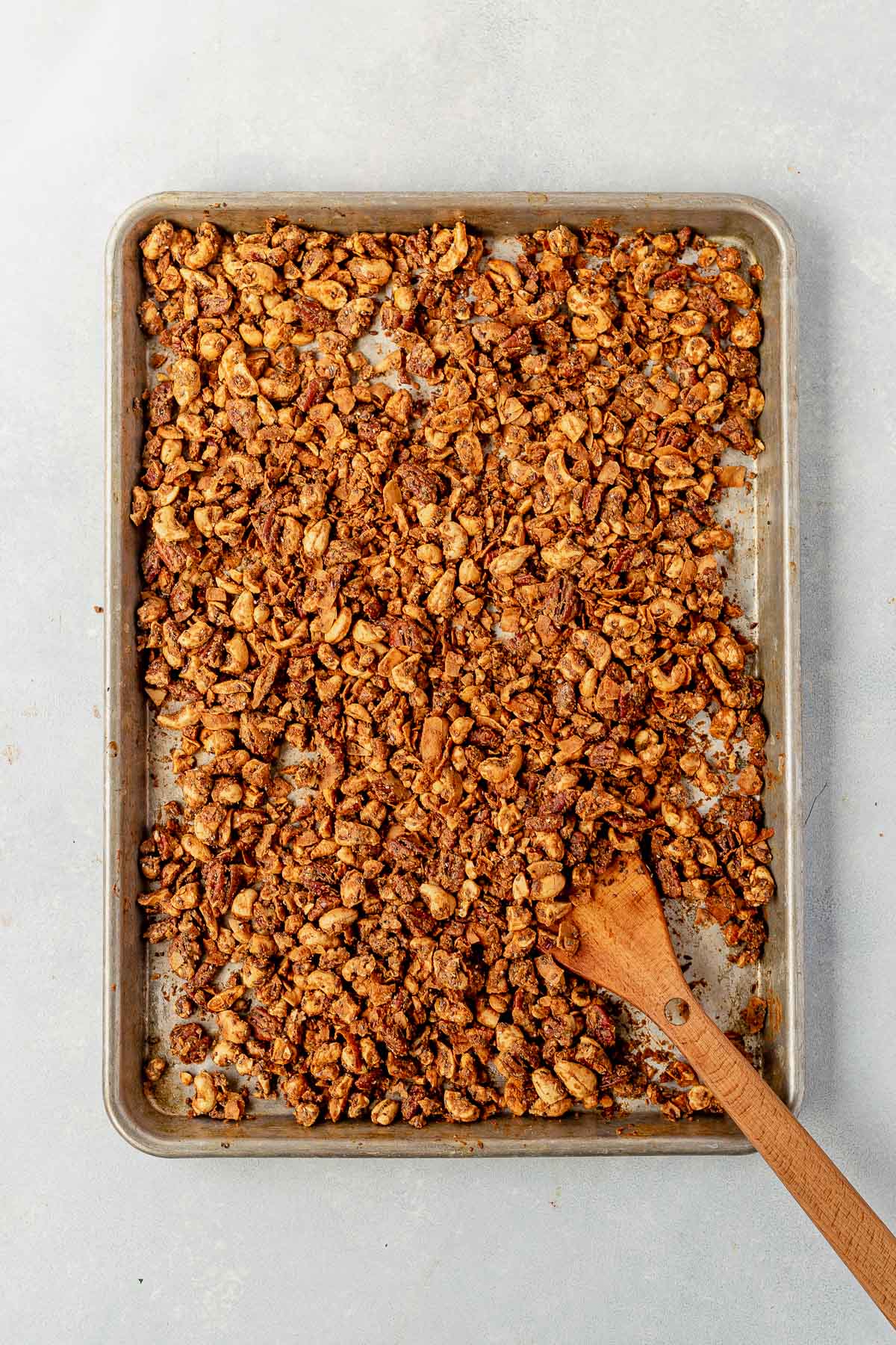 grain free granola spread out on a large sheet pan with a wooden spoon