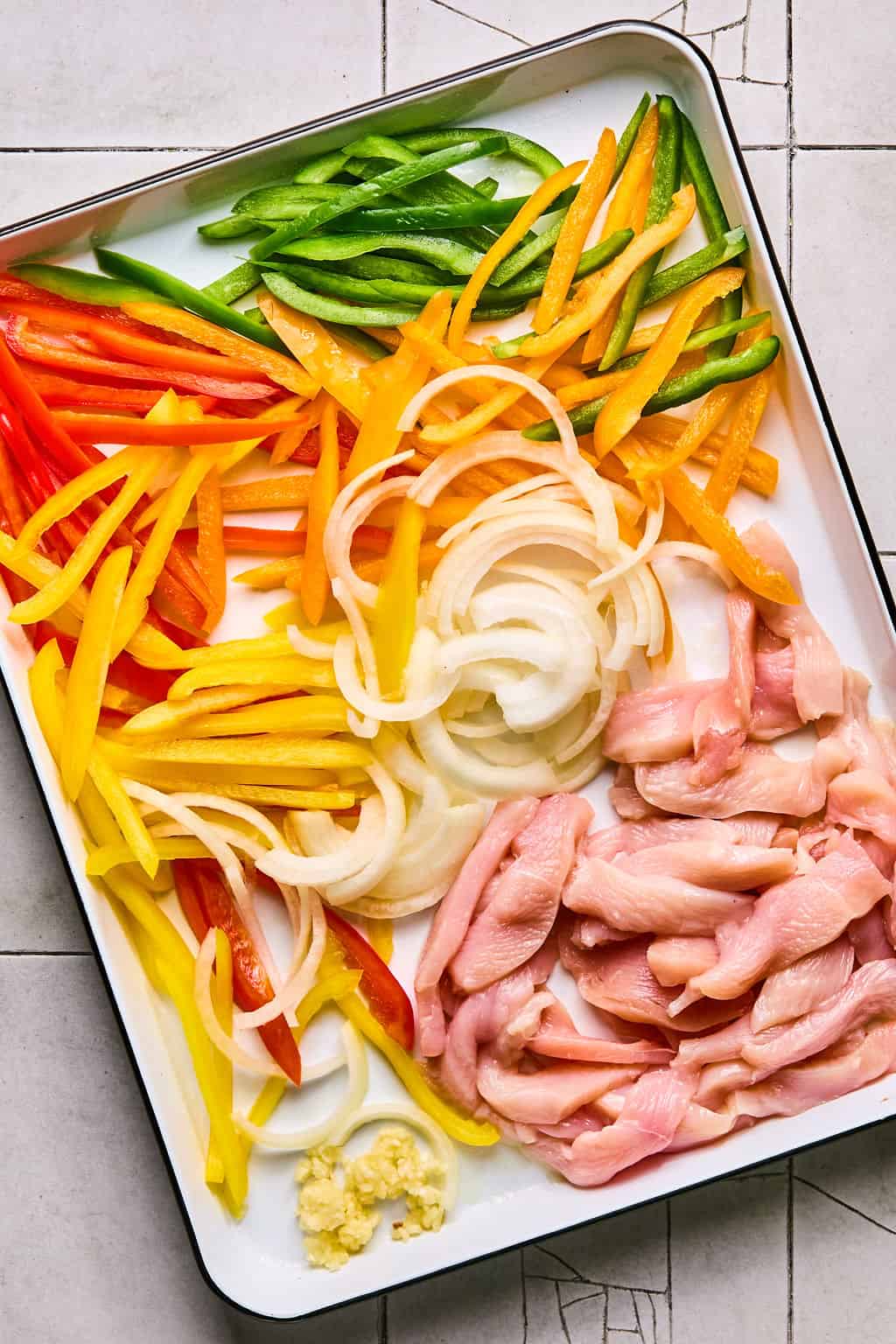 sliced chicken, onion, and peppers on a sheet pan.