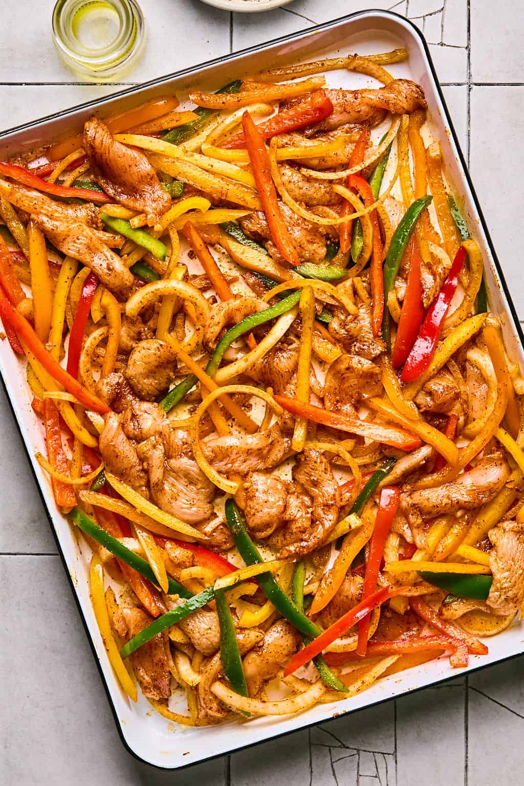 sliced chicken, peppers, and onions tossed in fajita seasoning on a sheet pan.