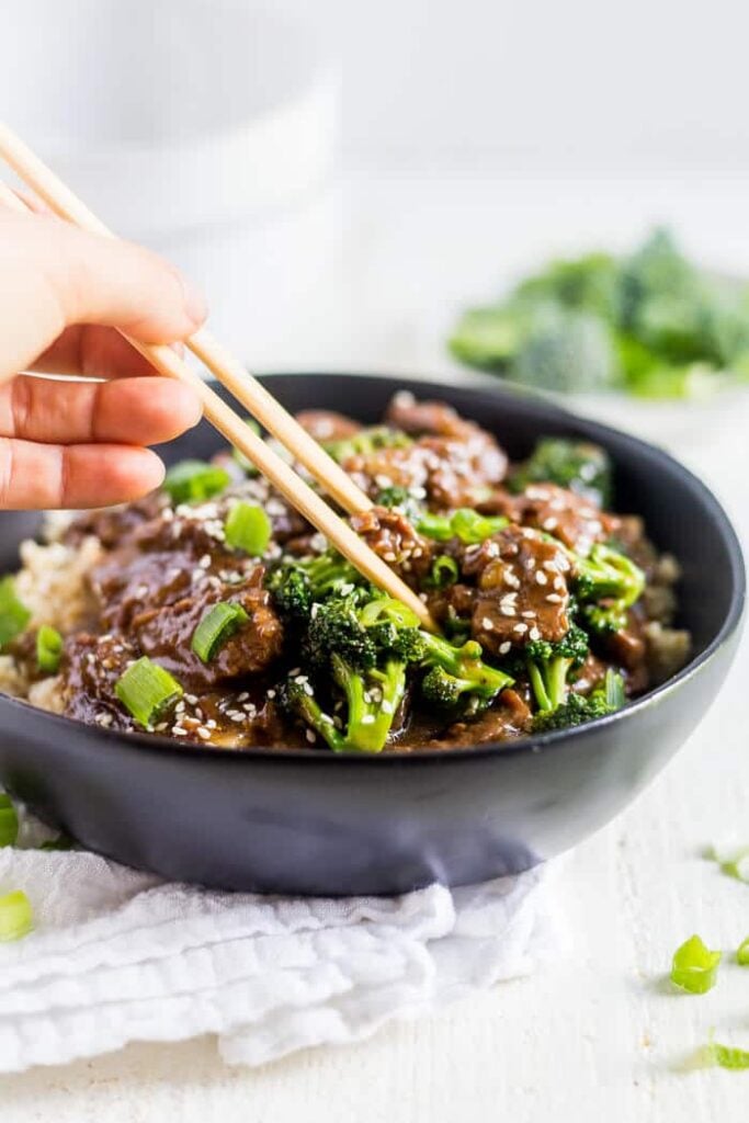 hand and chopsticks grasping instant pot mongolian beef in a shallow black bowl
