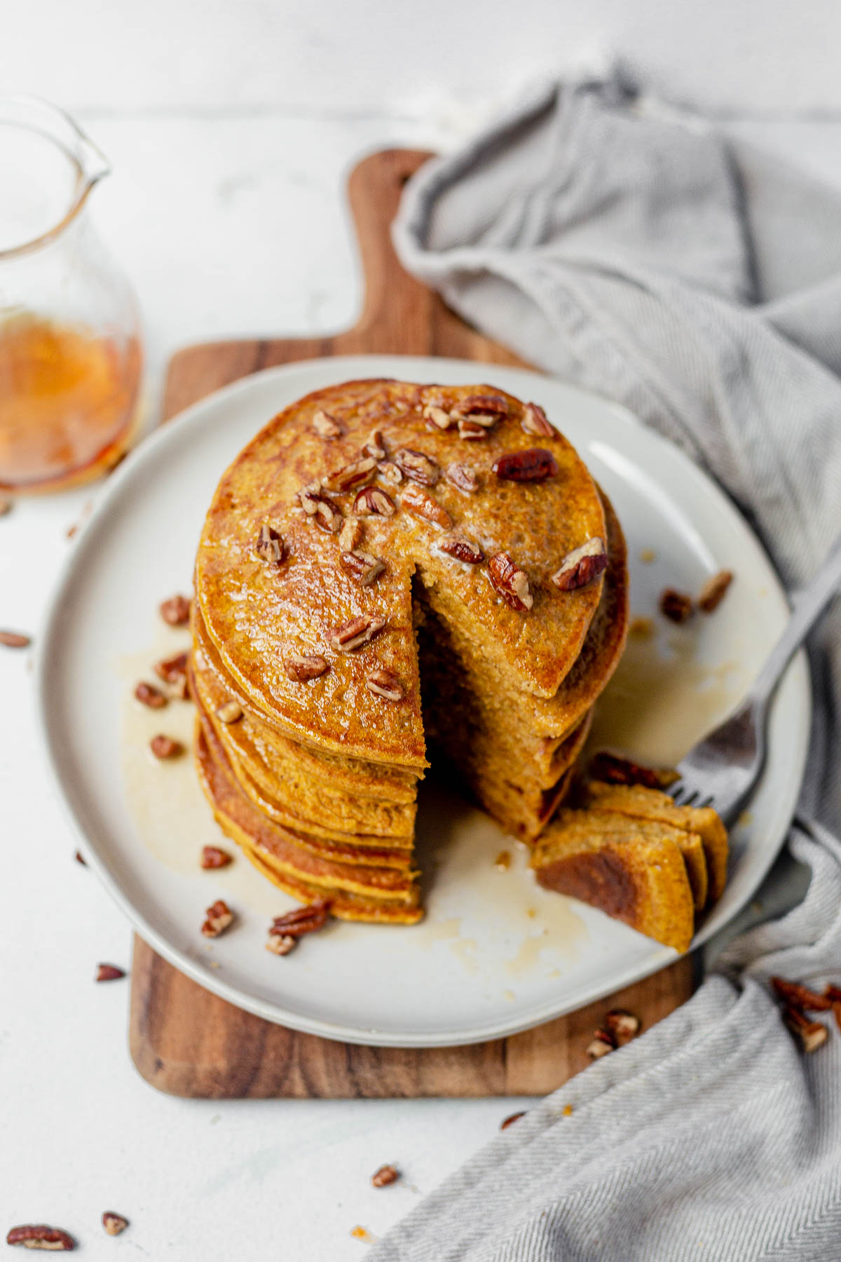 healthy pumpkin pancakes on a white plate topped with pecans and maple syrup