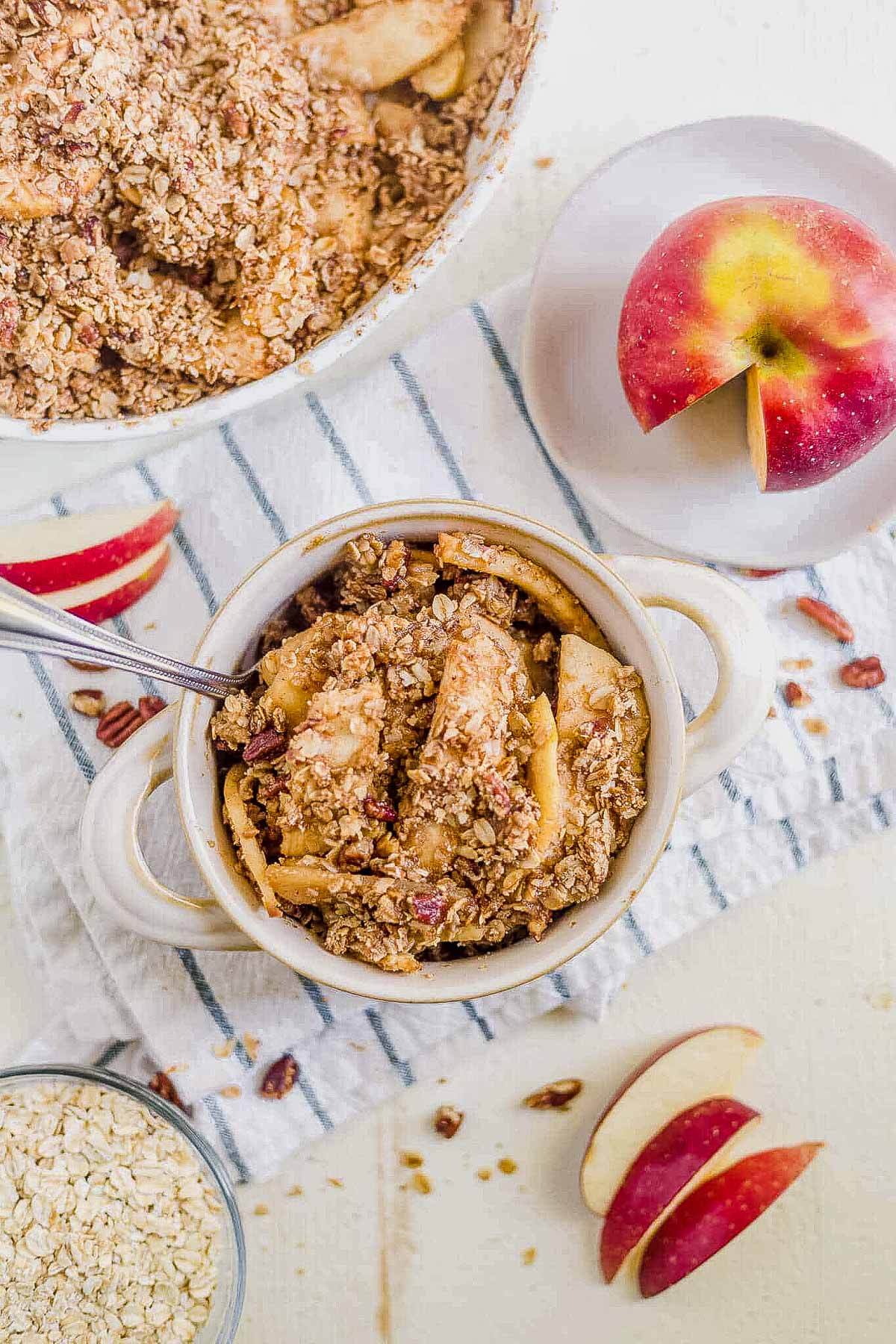 healthy apple crisp in a white bowl with sliced apples on the side