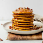 healthy pumpkin pancakes stacked on a white plate with syrup drizzling down the side