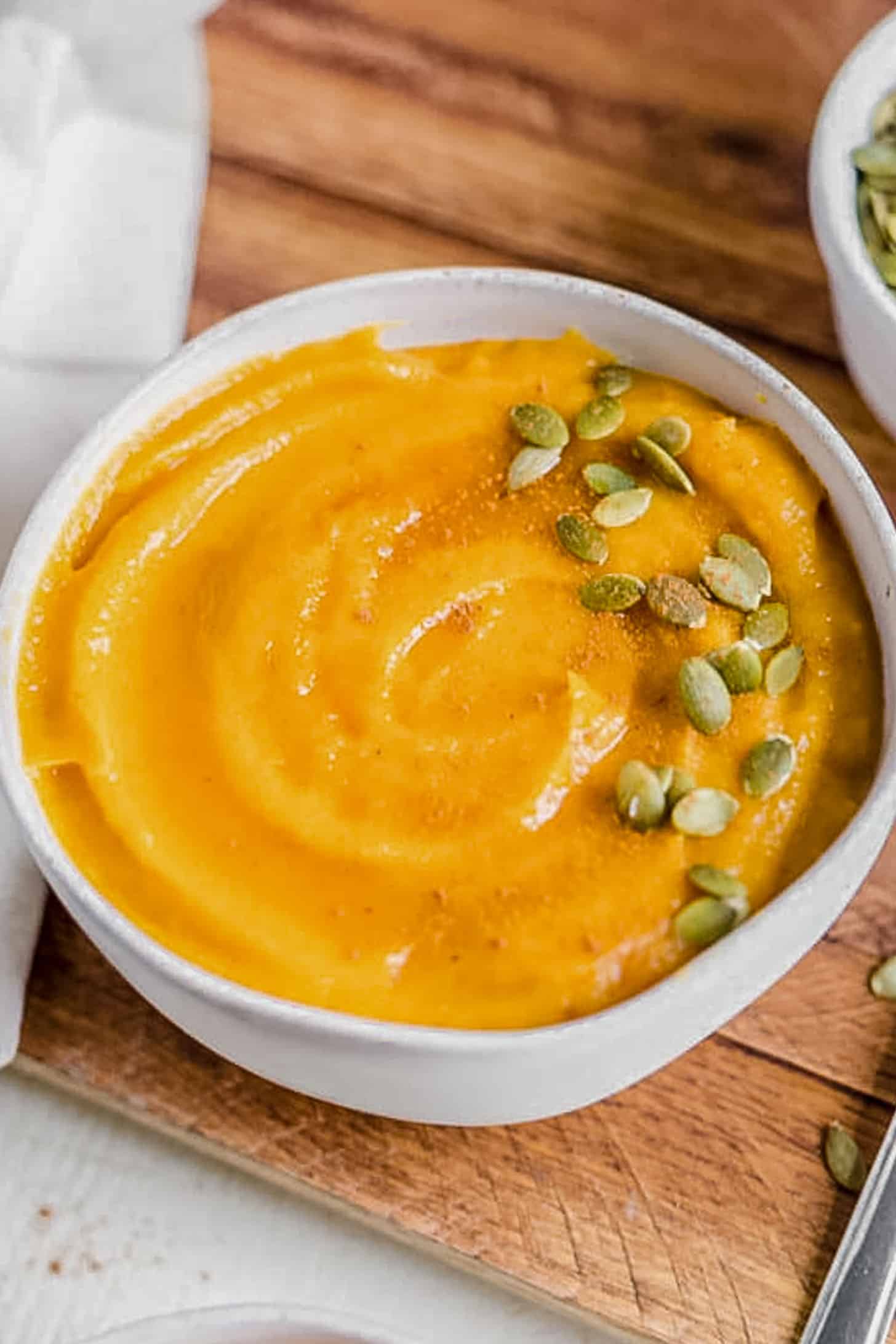 pumpkin seeds on top of a bowl of butternut squash soup
