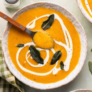 roasted butternut squash soup in a bowl with a spoon and crispy sage on top.