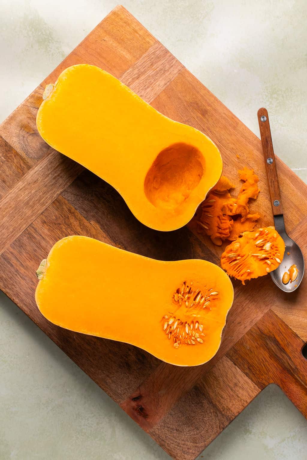 a butternut squash cut in half and scooping out the seedy centers.