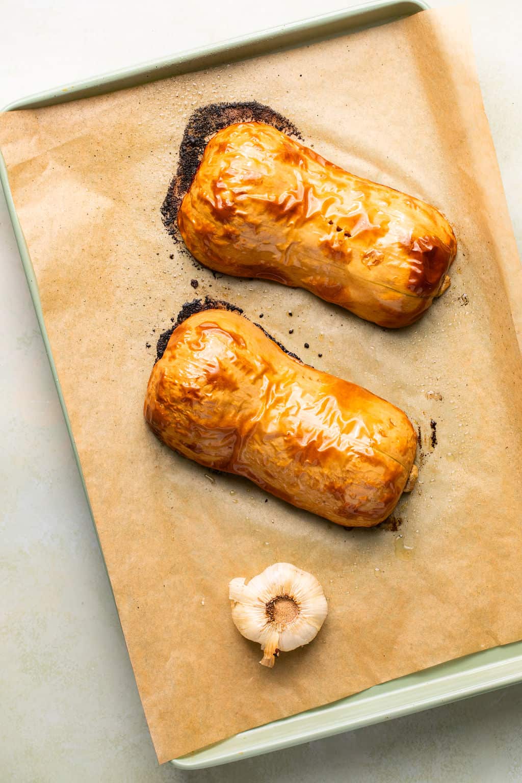 two halves of roasted butternut on a sheet pan with roasted garlic.