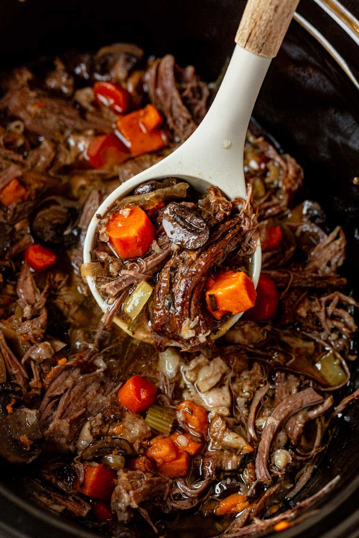 a ladle in a crock pot full of sweet potato beef stew.