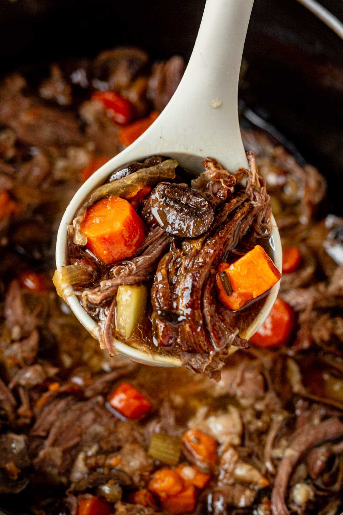 a ladle scooping sweet potato beef stew from a crock pot.