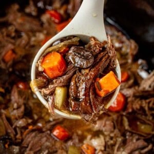 a ladle of sweet potato beef stew lifting out of the slow cooker.