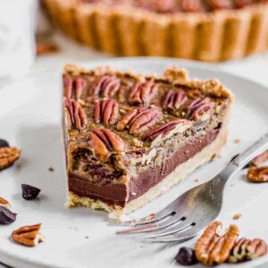 a slice of chocolate paleo pecan pie surrounded by chocolate chips and pecans