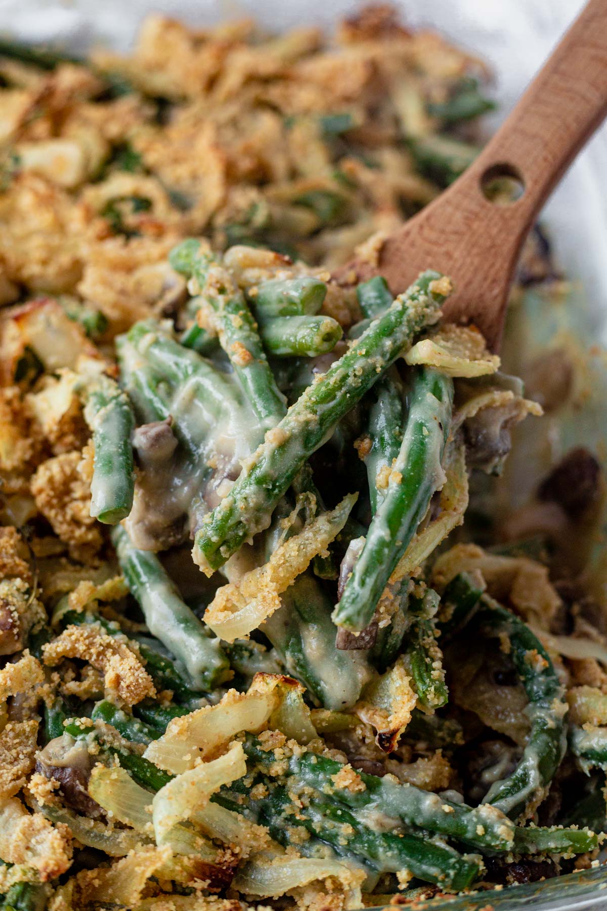 a wooden spoon scooping out dairy free green bean casserole from a dish