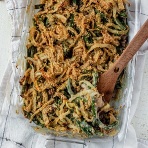 dairy free green bean casserole in a glass dish with a wooden spoon scooping some out