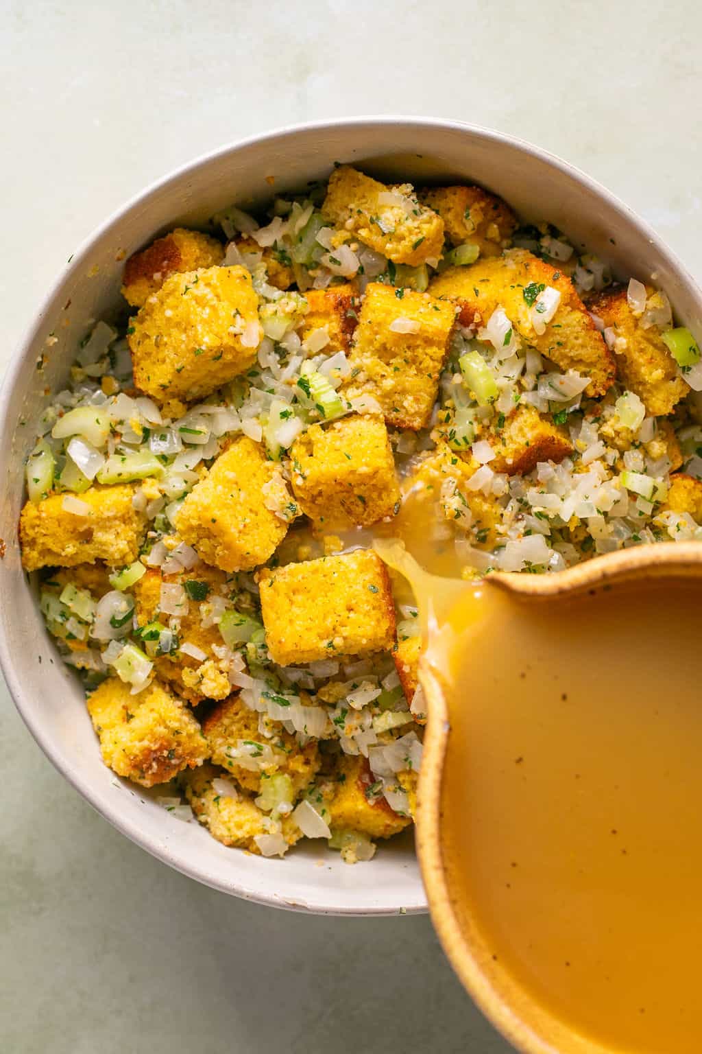 pouring broth over gluten free cornbread and cooked veggies in a bowl.