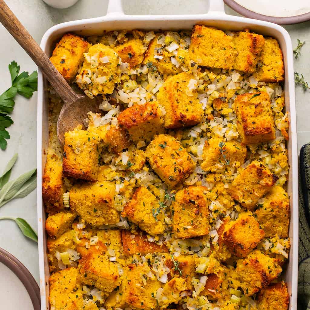 gluten free cornbread stuffing in a casserole dish with a wooden serving spoon.