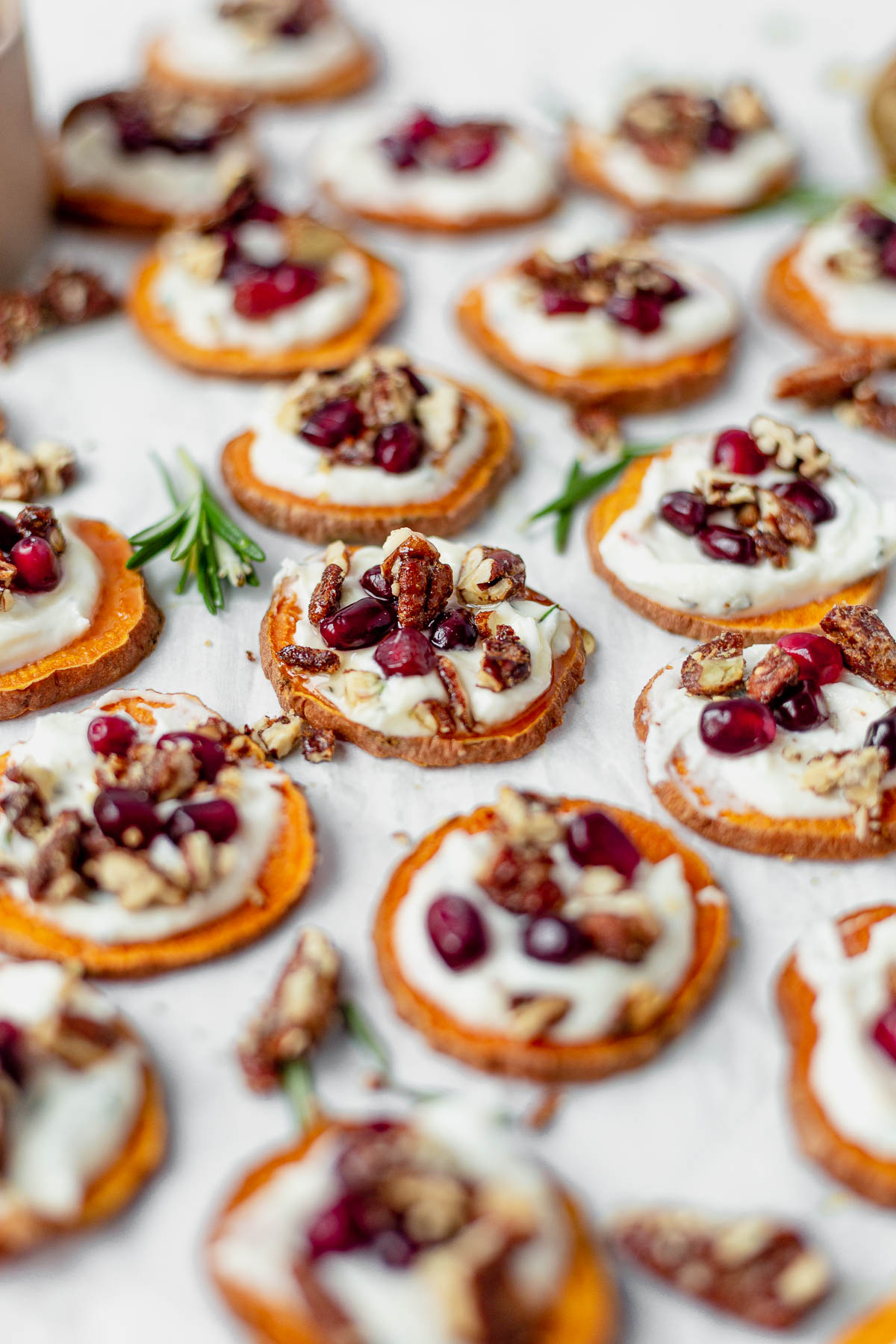 a sweet potato bite topped with pecans and pomegranate with fresh rosemary next to it