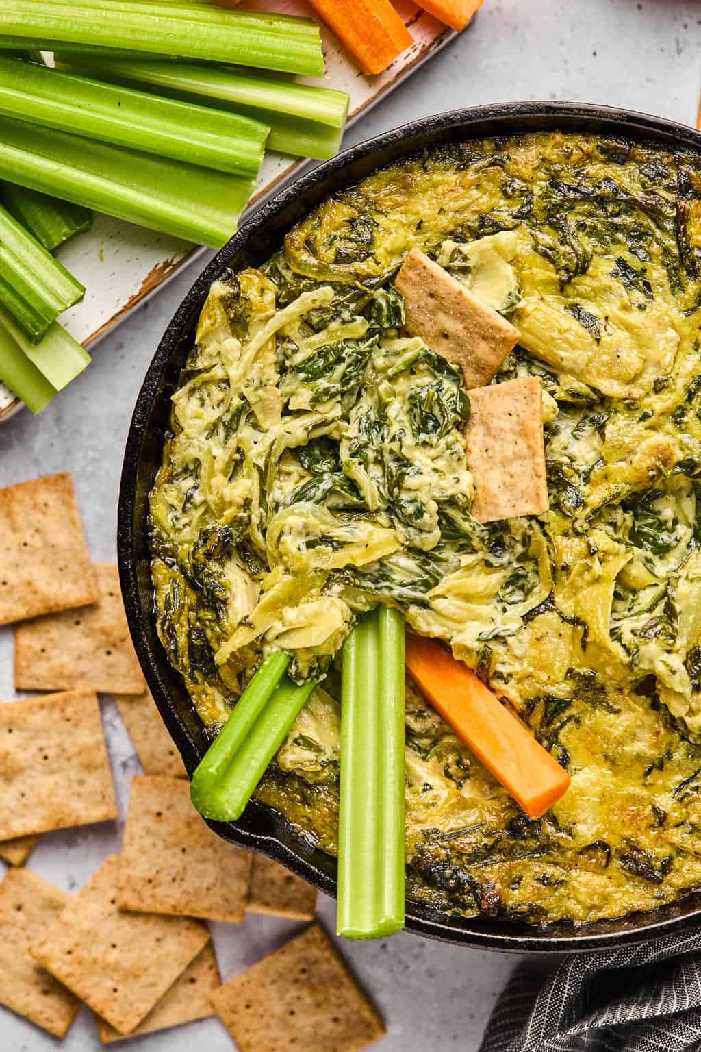 carrots and celery dipped into a skillet of dairy free spinach artichoke dip.