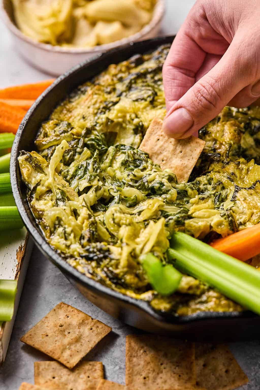 scooping dairy free spinach artichoke dip up with a gluten free cracker.