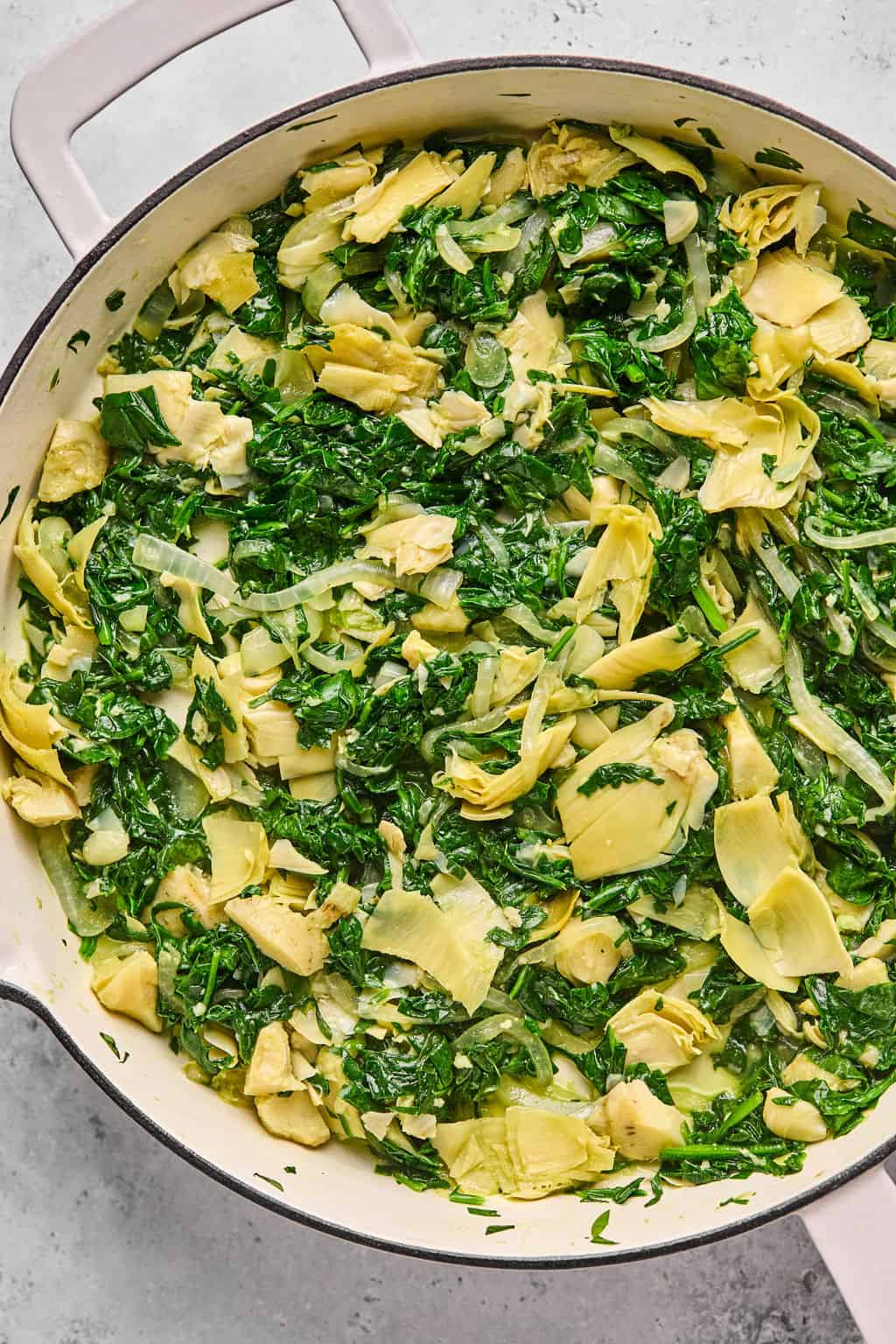 spinach, artichoke, and onion cooked in a skillet.