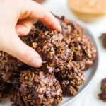 hand picking up a no bake chocolate oatmeal cookie off a plate of more cookies