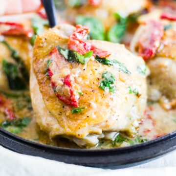 creamy tuscan chicken things in a cast iron skillet topped with basil